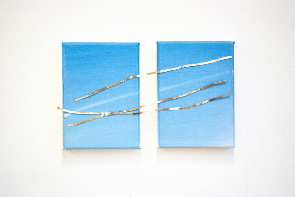 Art work 'We were meant to last' consisting of two blue paintings, with a white stripe across them. They are connected by three silver stripes, made out of sterling silver